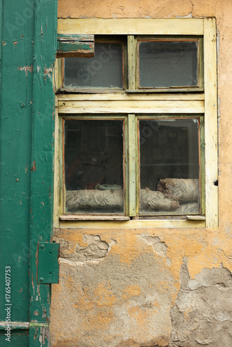 An old wooden window with dirty panes and peeling plaster on the old facade of a house. Architecture, city, neglect.