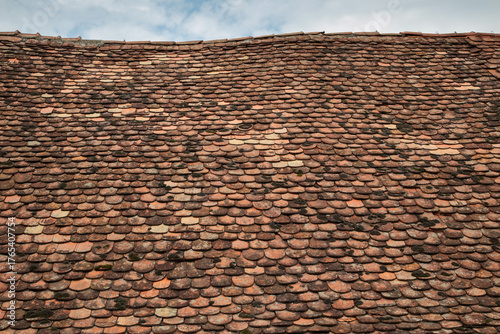 An old, undulating roof with old tiles, with a fragment of the sky with clouds in the background.