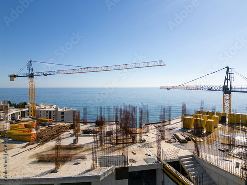 Aerial view of a construction site with tower cranes building modern apartments near the sea coast on a sunny day. Urban development concept