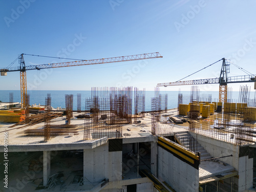 Aerial view of a construction site with tower cranes building modern apartments near the sea coast on a sunny day. Urban development concept