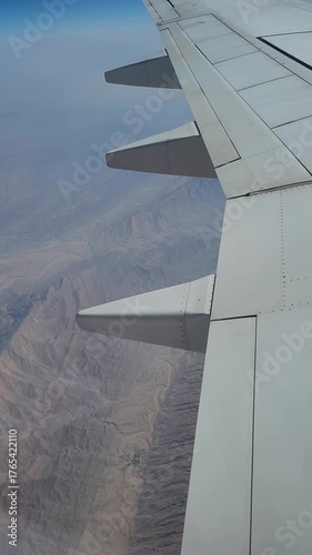 Airplane flying above rocky mountains, side window view