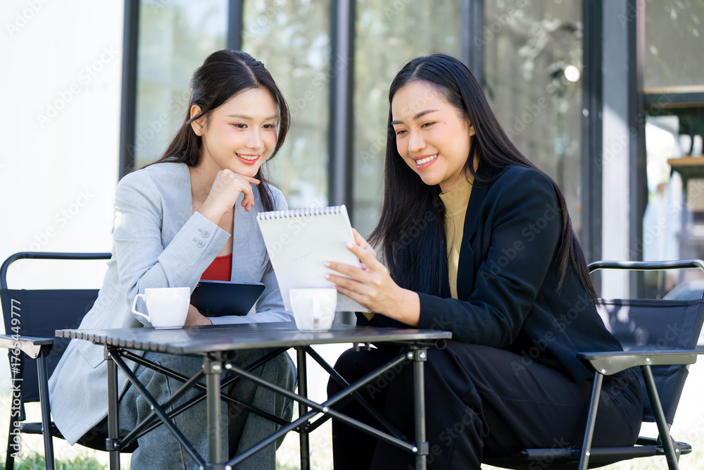 Obraz premium Two happy businesswomen collaborating on a project at an outdoor cafe.