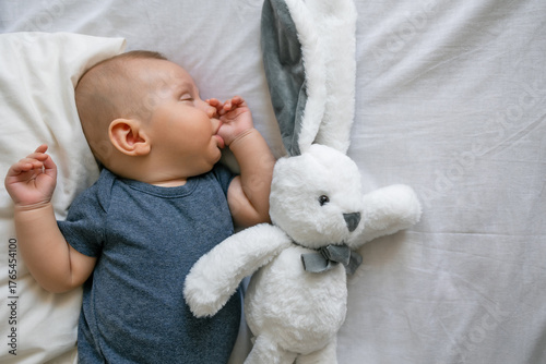 Sleeping cute baby boy sucking thumb finger with plush bunny rabbit toy on white blanket