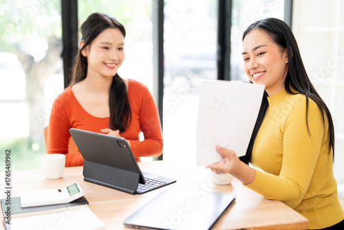 Free Download Two cheerful Asian businesswomen reviewing financial documents and collaborating on a project. - GFXLoad