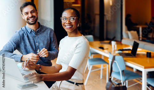 Two office colleagues smiling and working at a laptop computer in a shared space