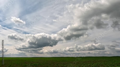 Beautiful endless clouds fly over a green field. 4K video (Ultra High Definition) of cloudscape and bright sun. Sky and clouds Timelapse. Sun shines through the clouds on the blue sky background.