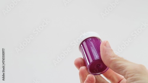 Mano che regge un flaconcino di tempera acrilica di colore viola chiaro, lilla su sfondo bianco - inquadratura ravvicinata
