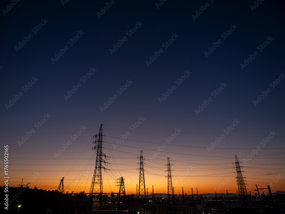 Obraz premium 夕焼け空と都市の風景。街並み。鉄塔と電線。オレンジ色から濃紺へのグラデーションの空。日没。横構図。広いコピースペース
