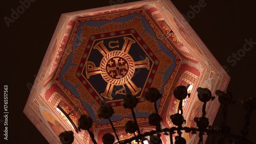 An ornate ceiling painting with religious symbols and bright colors inside an Orthodox temple. The chandelier silhouette adds depth and solemn beauty to the sacred interior.
