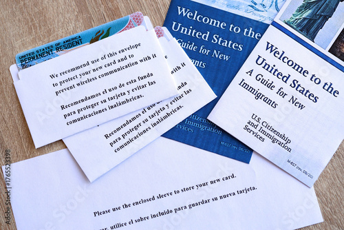 Permanent resident green card in envelope and guide for new immigrants lies on wooden table close up