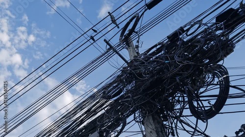 Messy tangled electrical power cables and wires on utility pole against blue sky showing chaotic infrastructure