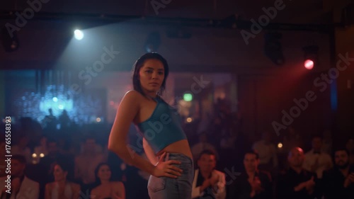 A dancer captivates the audience with her skillful movements under bright lights in a lively nightclub atmosphere. Colorful beams create a vibrant experience