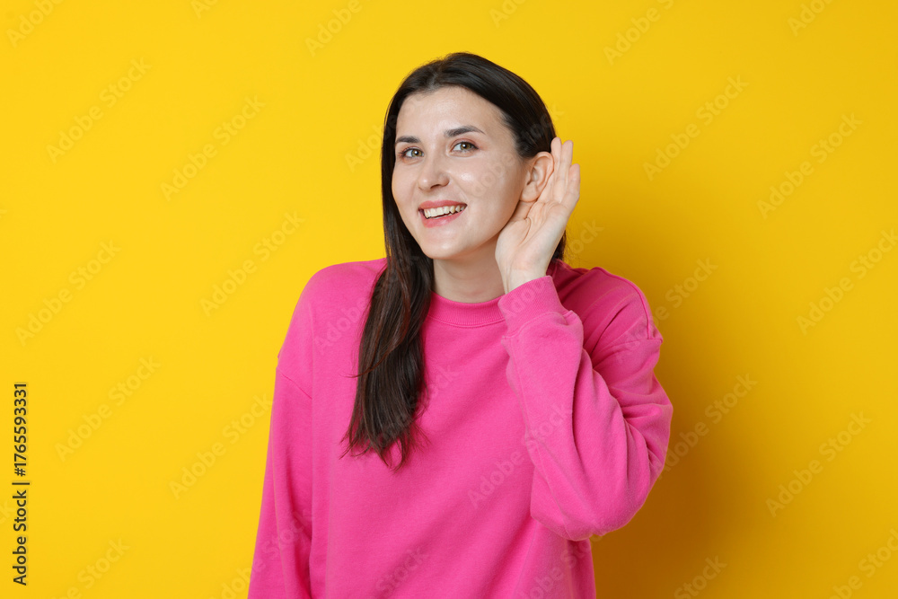Fototapeta premium Smiling woman showing hand to ear gesture on yellow background