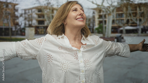 Photography Woman wearing a white blouse opens arms and tilts her head upward on an urban street lined with buildings; joy bliss delight happiness elation pleasure cheer glee contentment jubilation