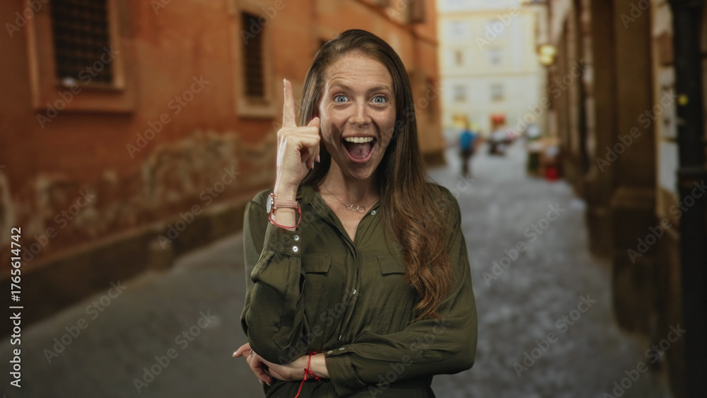 Fototapeta premium Woman points finger up on a cobblestone street with crossed arms and visible necklace; inspiration curiosity.