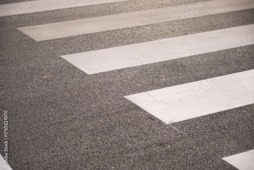 Close-up of a pedestrian crosswalk showing white zebra stripes painted on textured asphalt, highlighting road surface details, contrast, and urban street safety and minimal composition.