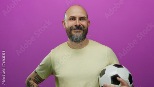 Foto Bearded man smiling confidently with a soccer ball against a vibrant pink background