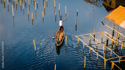 Aerial view of a solitary boatman navigates the still waters amidst a forest of wooden poles, creating a mesmerizing dance of light and shadow, Lagos, Lagos, Nigeria.