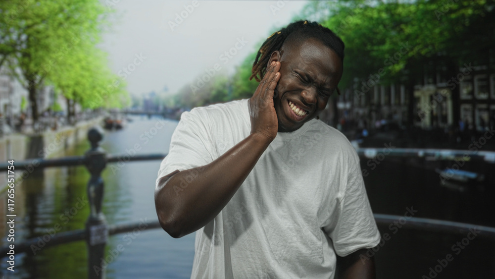 Φωτογραφία Man with hand on cheek for toothache on street canal bridge wearing white shirt and teeth clenched; pain struggle