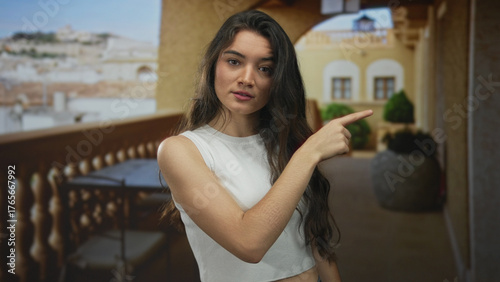 Canvas Print Woman in white tank top pointing finger to side in sunlit building hallway with serious gaze; rejection