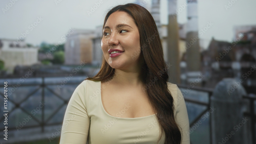 Fototapeta premium Young hispanic woman smiling and pointing with hand towards roman ruins by a building outdoors in sunlight; joy.