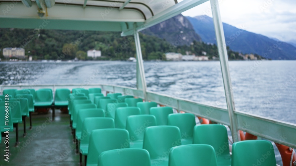 Obraz premium Empty ferry deck with rows of teal plastic seats in shallow focus, blurred lakeshore and distant mountains provide soft bokeh outdoor; background backdrop copyspace calm.