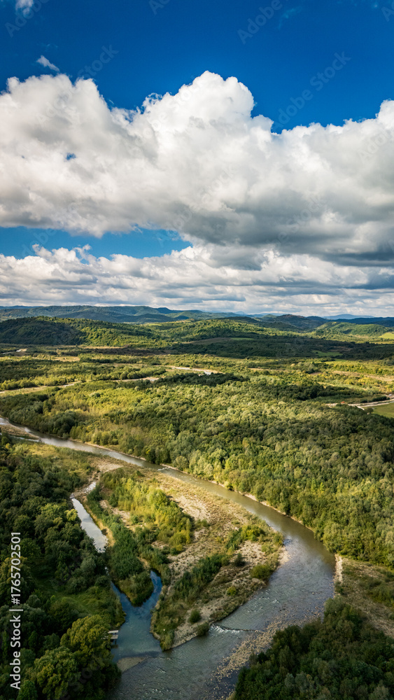 Fototapeta premium Aerial drone photo of rocky hill covered with dense green forest and calm river below — peaceful landscape and natural harmony of western Ukraine