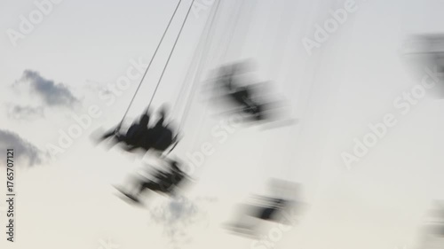 Abstract swing ride captured with low shutter speed, creating heavy motion blur against a pale sky. Dreamlike, surreal, and experimental imagery evoking freedom, speed, and disorientation.
