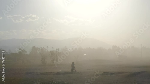 Silhouettes of people walking along a beach during a sandstorm. Dust and haze cover the landscape, creating a dramatic, atmospheric scene of resilience and harsh natural conditions.