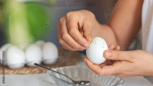Close-up shot of woman hands peeling shell of boiled egg on the table