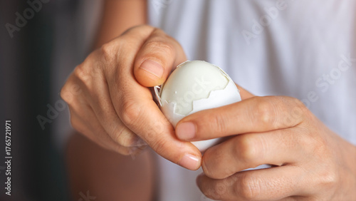 Close-up shot of woman hands peeling shell of boiled egg on the table