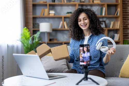 Canvas Print Young woman smiling, presenting new wireless headphones from an open cardboard b