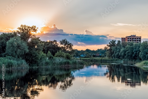 Dramatic sunset over Khorol River in Myrhorod, Poltava region, Ukraine with golden clouds, perfect water reflections and lush riverbank vegetation. Beautiful evening light creates serene atmosphere