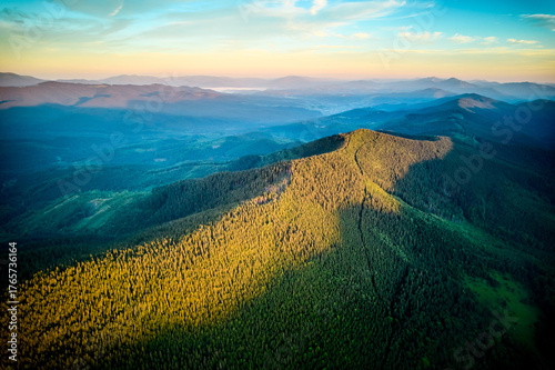 Valokuva Aerial view of sunlit forested mountain with long shadows casting across vibrant green trees