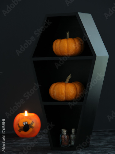 Halloween decorations in a spooky black coffin with pumpkins and a decorative orange lighted candle beside it with a dark background with copy space.