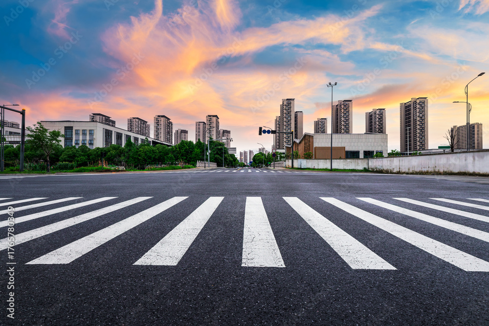 Obraz premium Empty city street intersection with crosswalk markings and modern residential buildings in the background at sunset.