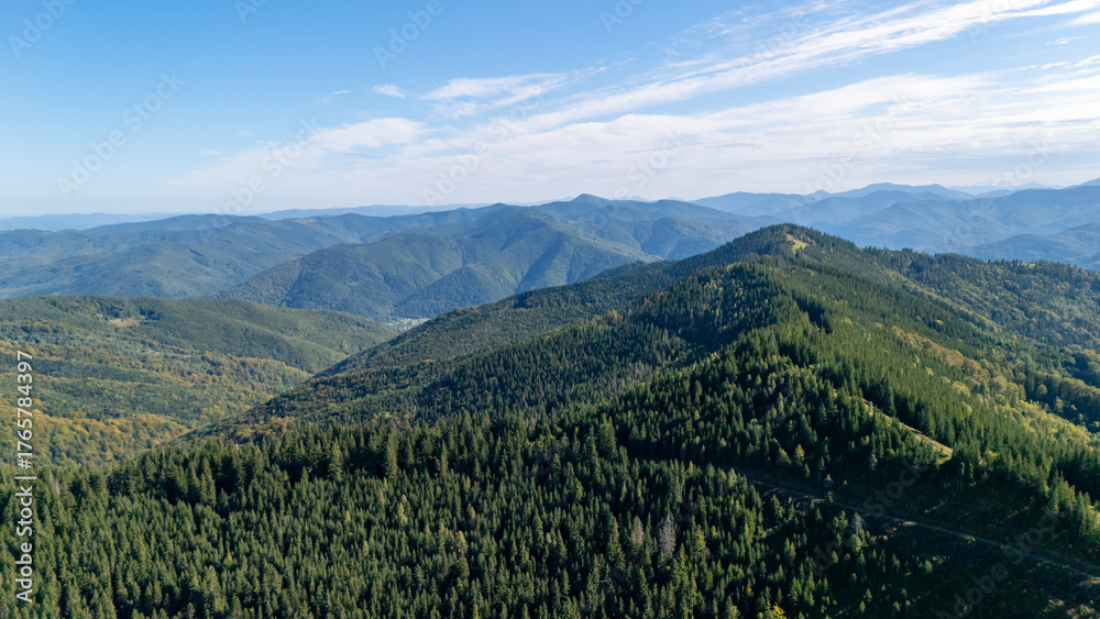 Naklejka premium Breathtaking aerial view of Carpathian mountains with sunlit forests and rolling hills under a partly cloudy sky, symbolizing freedom and nature’s calm