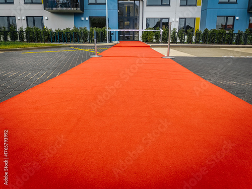 A wide red carpet leads to the entrance of a contemporary blue and yellow apartment complex, creating a formal and welcoming atmosphere. Ample copy space in foreground.