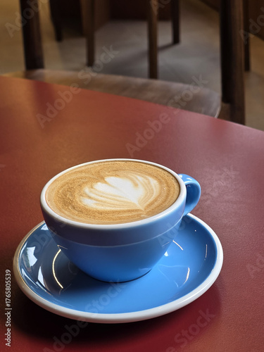blue coffee cup with latte art sits on red table, creating cozy atmosphere perfect for enjoying warm beverage