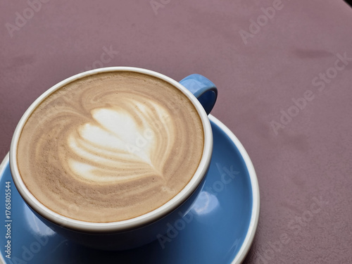 beautifully crafted latte with heart shaped foam design sits in blue cup on pink surface, inviting warmth and comfort