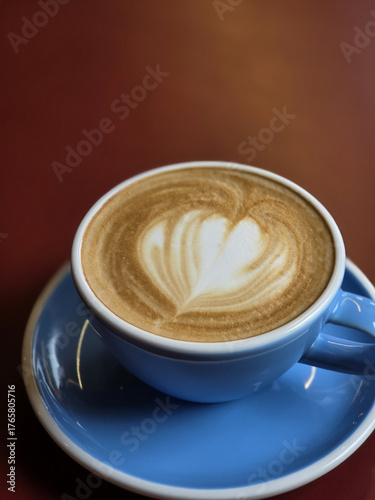 beautifully crafted latte in blue cup, showcasing intricate foam art on top. warm tones of coffee contrast with vibrant cup, creating cozy atmosphere