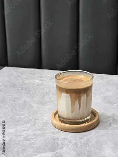 glass of coffee on wooden coaster, placed on marble table with dark background. warm tones of coffee contrast with cool surface, creating cozy atmosphere