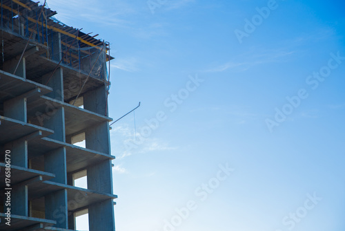 A partially constructed concrete building on the construction site with scaffolding and a bright blue sky, highlighting architectural progress and development. The concept of construction of an