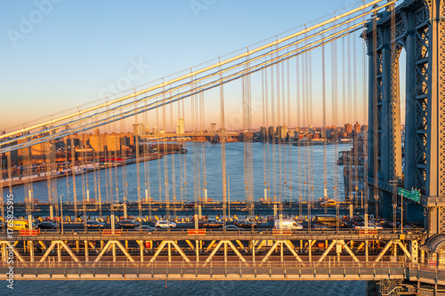 Aerial view of the iconic Manhattan Bridge, its steel cables gleaming in the soft light above the East River, traffic flowing steadily towards distant buildings, Manhattan, New York, United States.