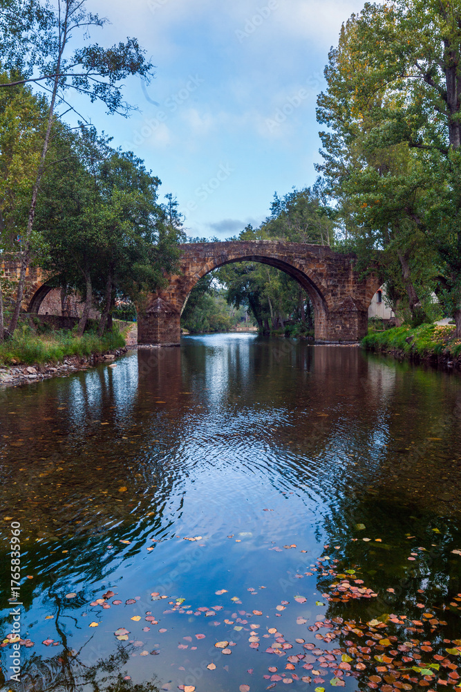 Fototapeta premium A historic stone arch bridge spans a calm, clear river
