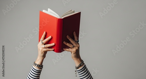 Close-up showing a person reading a bright red book with the pages fanned open against a plain wall.