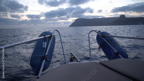 Sea boat yacht sailing travel approaching dramatic rocky coastline over choppy dark water at twilight