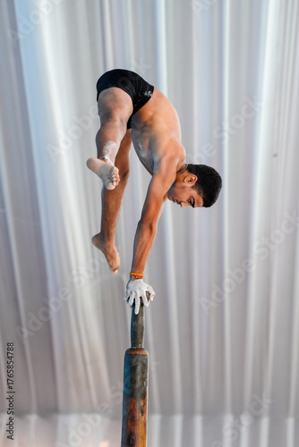 Young male athlete performing a handstand on top of a vertical wooden pole, showcasing Mallakhamb skills, strength, focus, and exceptional balance and core control.