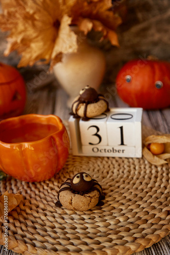 Autumn Halloween still life - funny cookies in shape of spider and cup of tea in shape of pumpkin. 31 of October on calendar