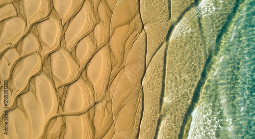 Aerial view of intricate natural patterns on golden sand, sculpted by receding turquoise ocean water. A serene, abstract coastal landscape where land meets clear sea beautifully